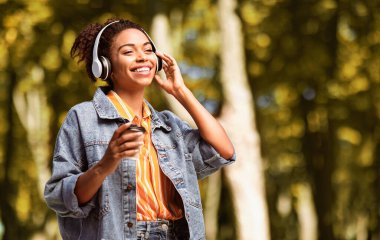 Sonbahar Hafta Sonu. Kulaklık takan, müzik dinleyen, parkta kahve içen Afro-Amerikan bir kız. Boş Boşluk