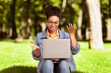 Neşeli Siyah Bağımsız Kadın dizüstü bilgisayar kullanarak Green Park 'ın dışında otururken görüntülü arama yapıyor. Her Zaman Dokunaklı Kavram