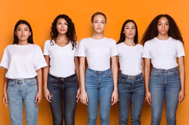 Beş ciddi çok ırklı kadın grubu arka arkaya poz veriyor ve sarı arka plan, stüdyo çekimlerine bakıyorlar. Kadın Çeşitliliği ve Birlik Konsepti