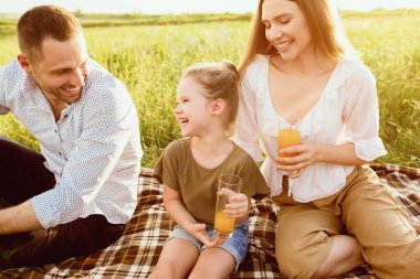 Güzel bir gün. Gülen ailenin portresi battaniyeye oturmuş taze meyve suyuyla piknik yapıyor.