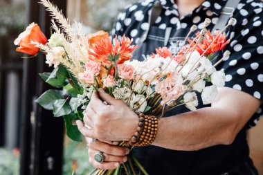 Çiçek kompozisyonu profesyonellerin elinde. Önlüklü kadın, elinde aletlerle çiçekçi dükkanının içinde buket yapıyor.