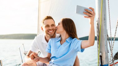Yat Sürüşü Macerası. Sevgili çift telefonda Selfie çekiyor. Deniz kenarında yaz tatilinin tadını çıkarıyorlar. Mutlu koca ve eş, açık denizde romatik bir gemi gezisi yapıyorlar..