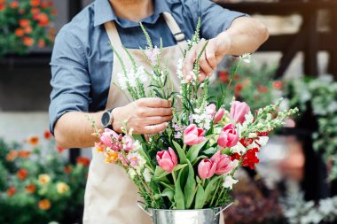 Çiçekçi çiçek buketi düzenler. Önlüklü ve koruyucu maskeli meşgul genç erkek müşteriler için çevrimiçi olarak dekoratif bitkilerle, boş alanlarla, mağazada moda kompozisyonu oluşturuyor.