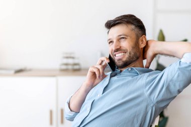 Memnun oldum. Yakışıklı bir ofis çalışanı cep telefonuyla konuşuyor, kahve içiyor, iş yerinde dinleniyor, sandalyeye yaslanıyor, boş bir alan yaratıyor.