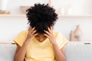 Çocuk bunalımı. Mutsuz siyahi kız kafaya dokunuyor depresif bir şekilde koltukta oturuyor evde sorunları var..