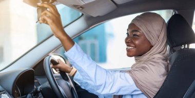 Yeni araba alıyorum. Hijab 'daki Müslüman Afrikalı Kadın Arka Ayna' yı ayarlıyor, Otomobili test ediyor, yeni aracının keyfini çıkarıyor, modern otomobilde sürücü koltuğunda oturuyor,
