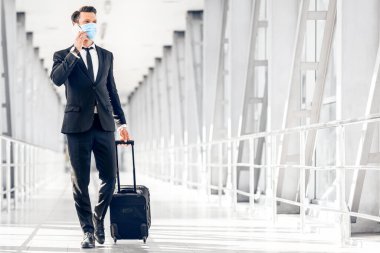 Zengin girişimci, havaalanının önünden bavulla geçerken telefonla konuşuyor.