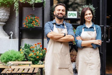 Çiçekçi açılışı, küçük işletme ve mağaza açılışı. Stüdyoda kollarını kavuşturmuş önlüklü genç ve sakallı Avrupalı bir adam ve güzel bir kadın. Ya da bitkilerle dolu bir eko kafe.
