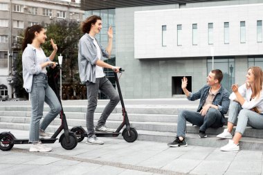 Çeşitli etnik çeşitlilikteki gençler birbirlerini selamlıyor, el sallıyor ve merhaba diyor, basamaklarda oturuyor ve bisiklet sürüyor.