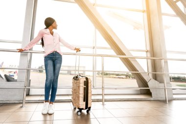 Seyahat Konsepti. Havaalanı Terminalinde, yanında bavuluyla bekleyen mutlu Afro-Amerikan Kadın, Koridorda Uçağı Beklerken Neşeli Siyah Kadın,