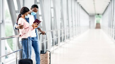 Havaalanındaki tıbbi maskeli siyah çift uçuş kapısına bakıyor, biletlere bakıyor, terminal koridorunda duruyorlar.