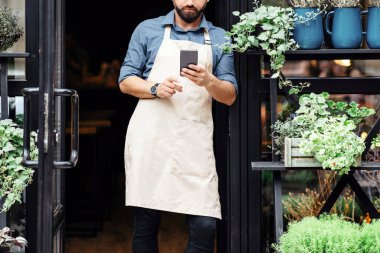 İnternetten çiçek siparişi vermek, kır çiçeklerinde bitki satmak. Önlüklü genç, çekici, sakallı bir adam. Dükkanın önünde akıllı bir telefonla vazo ve saksılarda farklı çiçekler yazıyor.
