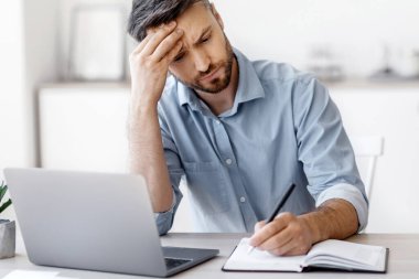 Ciddi Milenyum İşadamı Not alıyor ve modern ofiste dizüstü bilgisayar üzerinde çalışıyor, Girişimci Planlama İş Planlama Programı, Not Defterinde Yazıyor, Çalışma Masasında Oturuyor, Boş Alan