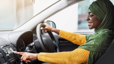 Tesettürlü Afrikalı Müslüman Kadın Arabayla Müzik Dinlerken Radyo İstasyonunu Değiştiriyor, Otomobil Ses Sistemi 'nin tadını çıkarıyor, Yeni Aracını test eden başörtülü İslamcı Kadın, Yan Görünüm