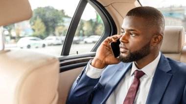 Siyah yönetici arabada arka koltukta oturuyor ve dijital tablet kullanıyor, e-postaları kontrol ediyor, telefon görüşmesi yapıyor, fotokopi çekiyor. Yakışıklı Afrikalı Amerikalı iş adamı toplantıya gidiyor, ofise giden yolda çalışıyor.