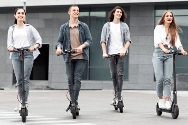 Tatilde dört şık zoomer şehirde elektrikli scooter sürerken eğleniyor.