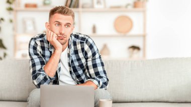 Can sıkıntısı kavramı. Kanepede dizüstü bilgisayarla oturan yorgun adam, yana bakıyor, geçmişi bulanık.