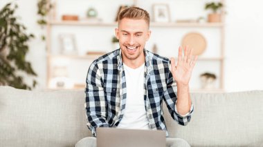 Sanal İletişim. Bilgisayarda video araması yapan, el sallayan, evdeki koltukta oturan heyecanlı insan.