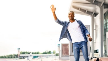 Geldikten sonra havaalanı yakınlarında taksiyi yakalayan yakışıklı siyahi adamın portresi bavul taşıyan gülümseyen Afrikalı Amerikalı genç adam ve taksi çağırmak için elini kaldırıyor.