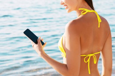 Bikinili Kadın Sahilde Açık Deniz 'in yanında Smartphone kullanıyor. Mobil Uygulama Konsepti.