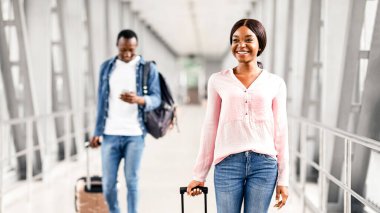 Travel Insurance Concept. Portrait Of Cheerful Black People Walking With Luggages In Airport Terminal, Happy African American Man And Woman Going Down To Plane, Enjoying Upcoming Flight, Free Space