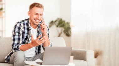 Müşteri Destek Konsepti. Akıllı telefondan konuşan, bilgisayarda çalışan oturma odasındaki kanepede oturan neşeli bir adamın portresi. Telekomünikasyon ve telesekreter. Kendine güveni tam bir erkek telefon görüşmesi yapıyor.