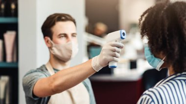 Girişte sıcaklık taraması. Güzellik hocası salonda bayan müşterinin ateşini ölçüyor.