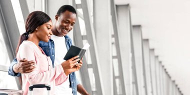 Ticket Sales Service. Portrait Of Happy Young Black Couple Waiting For Flight Boarding At Airport Terminal, Romantic African American Spouses Checking Passports And Tickets, Hugging And Smiling