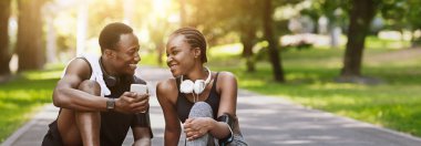 Açık havada antrenmandan sonra parkta dinlenen neşeli siyah atlet çift.