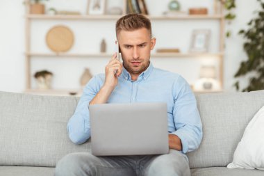 Akıllı telefondan konuşan ciddi bir çalışan dizüstü bilgisayarda çalışıyor koltukta oturuyor, kopyalama yapıyor.