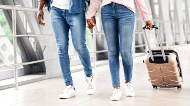 Hava Yolları Konsepti. Tanımlanamayan siyah çift, havaalanı terminalinde bavullarıyla dolaşıyorlar, uçuş kapısına gidiyorlar, Afrika kökenli Amerikalı eşlerin el ele tutuşup, birlikte seyahat etmelerinin keyfini çıkarıyorlar.