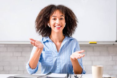 Modern teknoloji, sağlık koronavirüsten korur ve uzaktan evden çalışır. Kablosuz kulaklıklı neşeli Afro-Amerikan kadın oturma odasında İngilizce kurallarını anlatıyor.