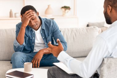 Psikoterapi kavramı. Terapi sırasında psikologla konuşan bunalımlı siyahi bir adam.