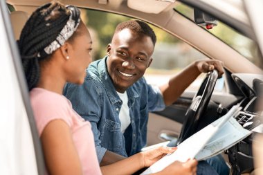 Birlikte araba gezisi yaparken harita okuyan mutlu siyahi gezginler yolun ortasında kayboldular, yan manzara, kopyalama alanı. Gülümseyen Afrikalı Amerikalı genç adam ve kadın yeni bir hedef arıyorlar.