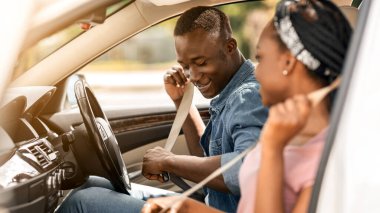 Güzel afro-amerikan erkek ve kadın lüks arabada emniyet kemeri takıyorlar, yaz tatiline otomobille gidiyorlar, mutlu siyahi aşıklar haftasonu gezisine çıkıyorlar, araba sürüyorlar, uzay kopyaları kopyalıyorlar.