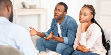 Duygusal Afrikalı bir adam, çift terapisinde eşiyle yaşadığı aile sorunlarından yakınıyor, ilgisiz eşinin yanında oturuyor.