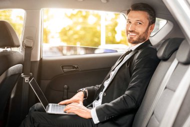Neşeli iş adamı arabada oturuyor, dizüstü bilgisayar kullanıyor, internette çalışıyor. Havaalanına giderken defter üzerinde çalışan takım elbiseli yakışıklı bir adam. İş kavramındaki modern teknolojiler