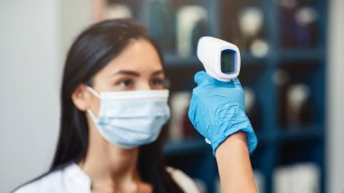 Müşteri sıcaklığı taraması. İşçi elinde ultra-ötesi ısı tarayıcısı olan kadın müşteri başı