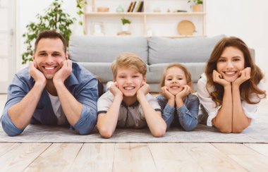 Çocukları yerde yatmış, kameraya gülümseyen genç bir aile. Ebeveynler ve Çocuklar Portresi.