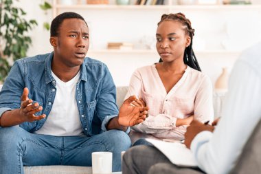 Duygusal siyahi adam evlilik terapisinde aile danışmanıyla konuşuyor, eşiyle olan ilişki sorunlarını anlatıyor, yanında oturan memnun olmayan kadın eşi, boş alan...
