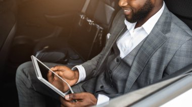 Gülümseyen zenci işadamı lüks bir arabada elinde boş ekranla dijital tablet tutuyor. Afro-Amerikalı neşeli bir adam iş seyahatini arabasıyla yaparken iş uygulamasını kullanıyordu.