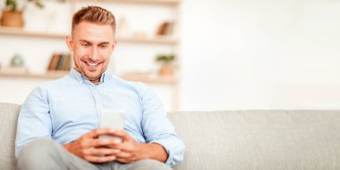 Sosyal Medya Haberleri Kaydırılıyor. Akıllı telefon tutan gülümseyen adamın yakın plan portresi, SMS mesajı yazmak, koltukta oturmak. İletişim Konsepti. Yetişkin adam internette geziniyor, komik videolar izliyor.