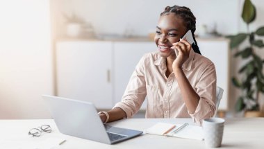 Ofiste cep telefonuyla konuşan, dizüstü bilgisayarla masada oturan, boş alan olan gülümseyen siyahi bir girişimci.