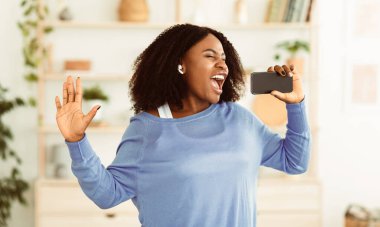 Kaygısız Şarkıcı. Afrikalı bir kadının portresi şarkı söylüyor ve cep telefonunu mikrofon olarak kullanıyor, dans ediyor ve kulaklık takıyor.