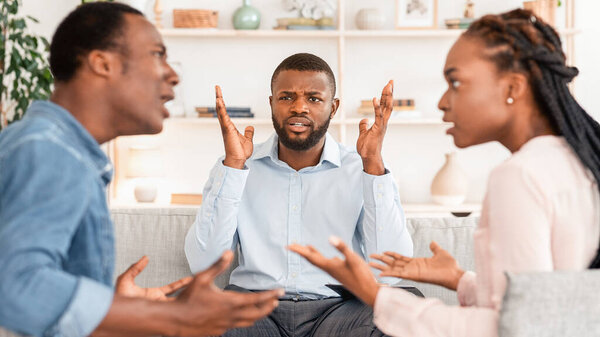 Раздражённый черный психолог наблюдает за парой споров во время сеанса супружеской терапии, не может справиться с конфликтом, африканские американские супруги ссорятся перед семейным психологом, избирательный фокус