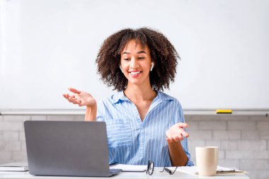 Evde kolay İngilizce dersleri. Dost canlısı, kablosuz kulaklıklı Amerikalı kadın dizüstü bilgisayara bakıyor ve kuralları anlatıyor.