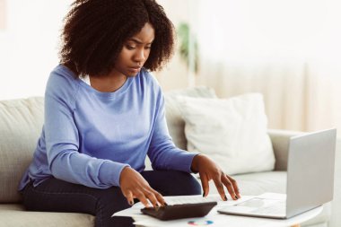 Bütçe Planlama Konsepti. Vergi hesaplayan ve evdeki koltukta dizüstü bilgisayar kullanan entellektüel siyah kadın.