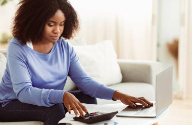 İş Muhasebe. Afrikalı iş kadını hesap makinesi kullanıyor ve dizüstü bilgisayarla çalışıyor. Boşluğu Kopyala