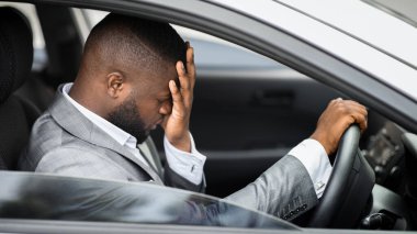 Üzgün Afro-Amerikalı iş adamı araba sürerken kafasını ovuyor. Takım elbiseli, yüzü avuçlarında, ofisten çıkıp giden, iş sorunları olan sinirli genç siyahi bir adam.