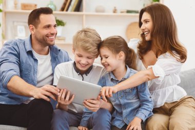 Ebeveynler ve çocuklar tablet bilgisayar kullanarak evde oturup film izliyorlar. Aile Hafta sonu Konsepti